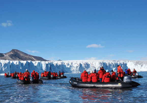 Kreuzfahrt-Gäste in roten Expeditions-Parkas fahren in Schlauchbooten entlang eines Gletschers in Spitzbergen
